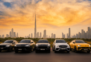 "Luxury cars including BMW, Lamborghini, Porsche, Mercedes, and Lamborghini Urus parked with Dubai skyline and Burj Khalifa in the background during sunset."