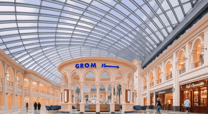 Luxury shopping mall interior with a glass-domed ceiling, elegant arches, and a central kiosk surrounded by patterned marble flooring.