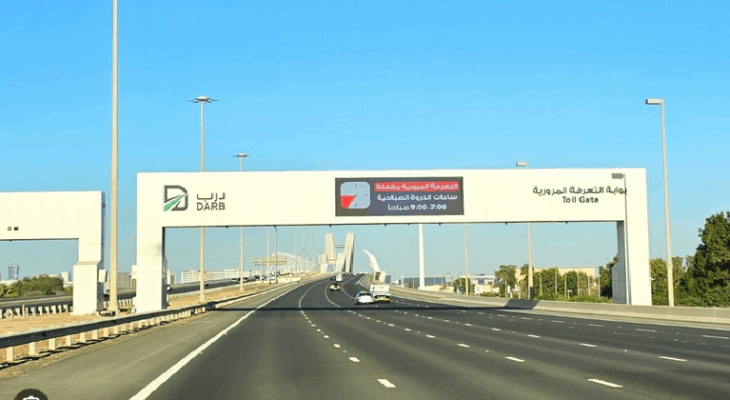 An overhead view of the DARB toll gate gantry spanning a busy, multi-lane highway in Abu Dhabi, with cars passing underneath.