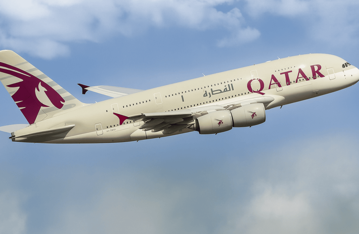 A Qatar Airways Airbus A380 aircraft is captured mid-flight against a partly cloudy sky, with the airline’s burgundy Oryx logo on the tail and engines, and the word "QATAR" prominently displayed on the fuselage.