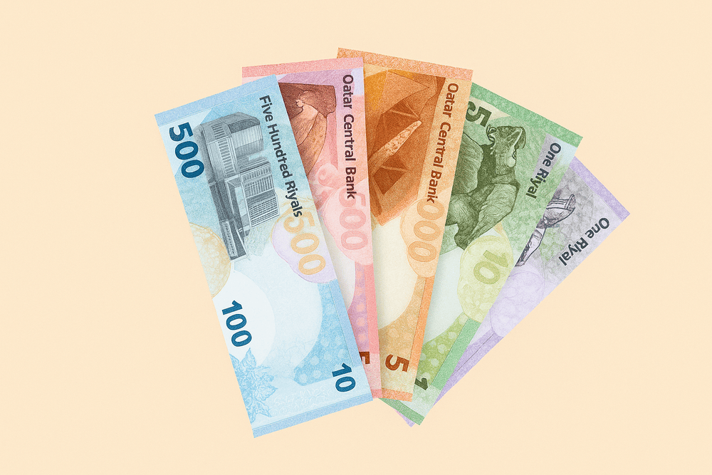 Six colorful Qatari Riyal banknotes arranged in a fan shape on a light beige background.